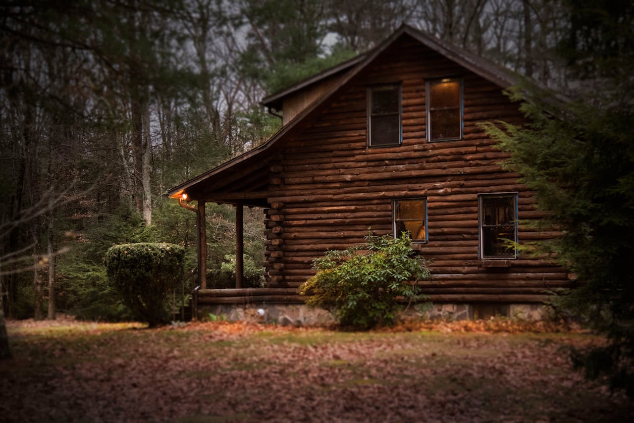 A cozy log cabin surrounded by autumn trees, showcasing warm lighting and tranquil nature.